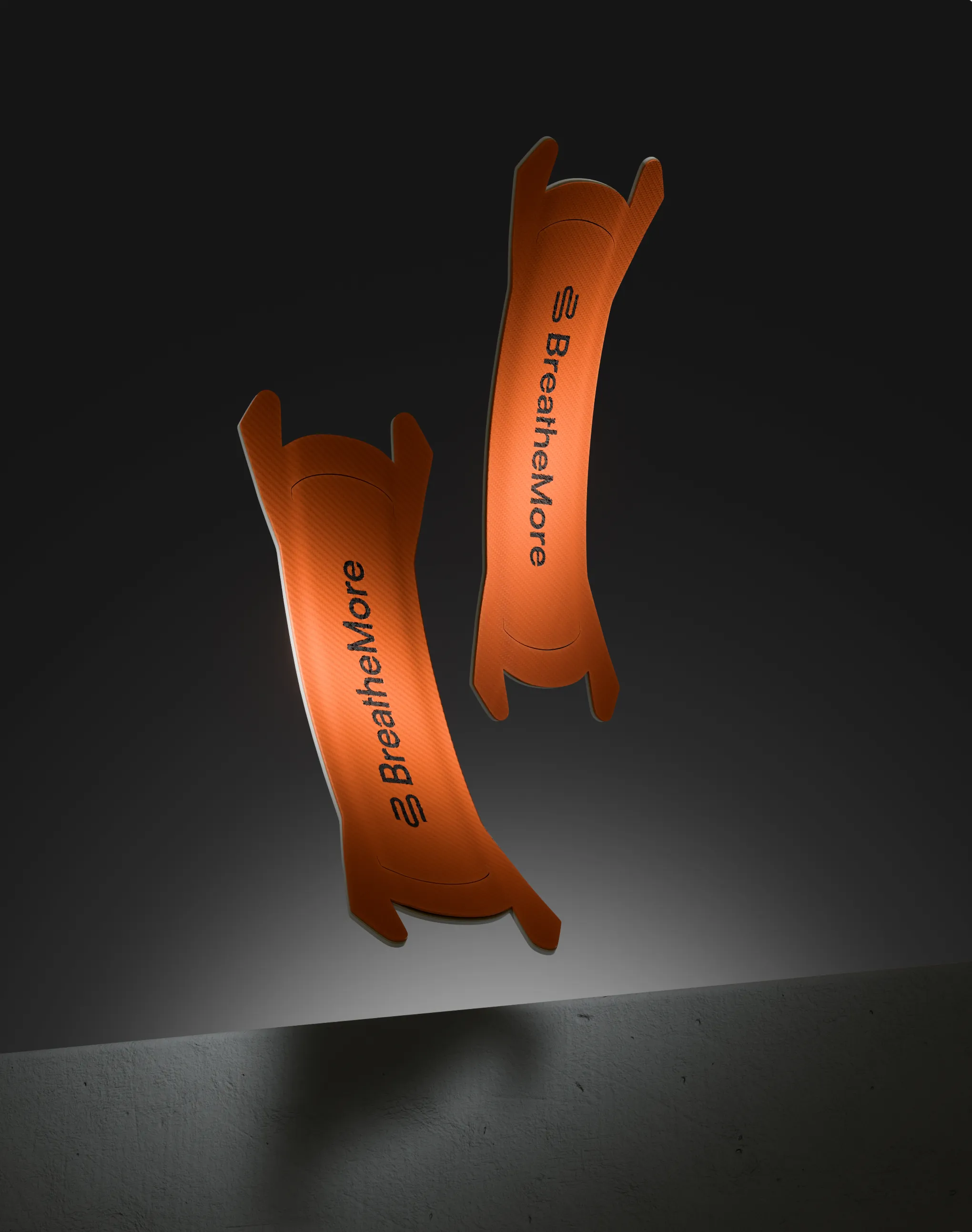 Two orange BreatheMore nasal strips suspended against a dark background