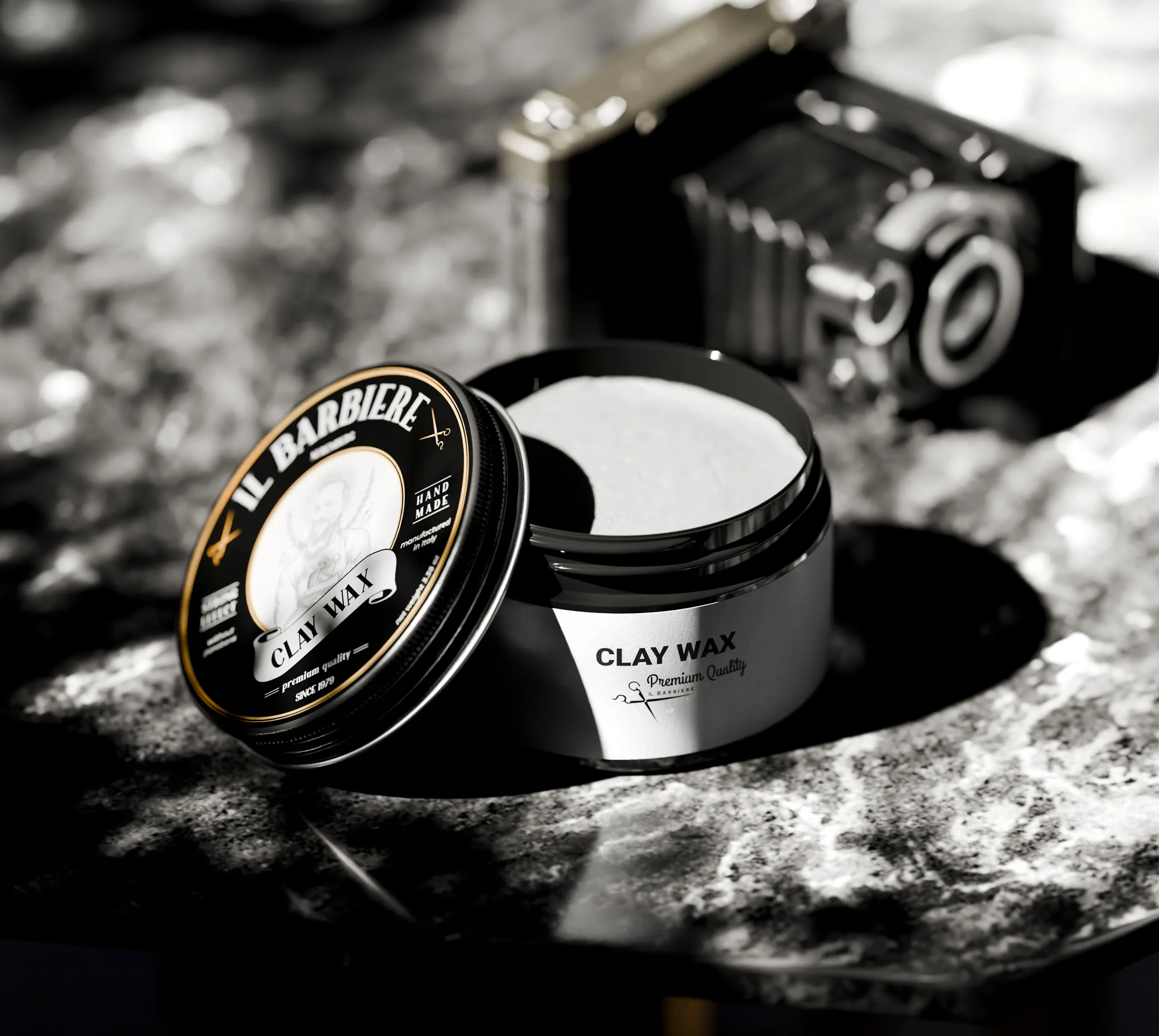 Open Il Barbiere clay wax jar and lid on textured stone beside a vintage camera