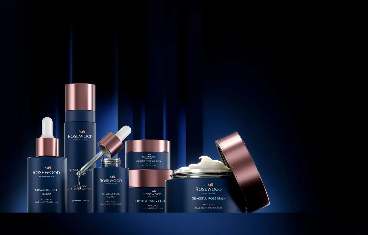 Rosewood skincare collection with navy bottles and jars, rose-gold closures and an open cream jar against blue-lit vertical panels
