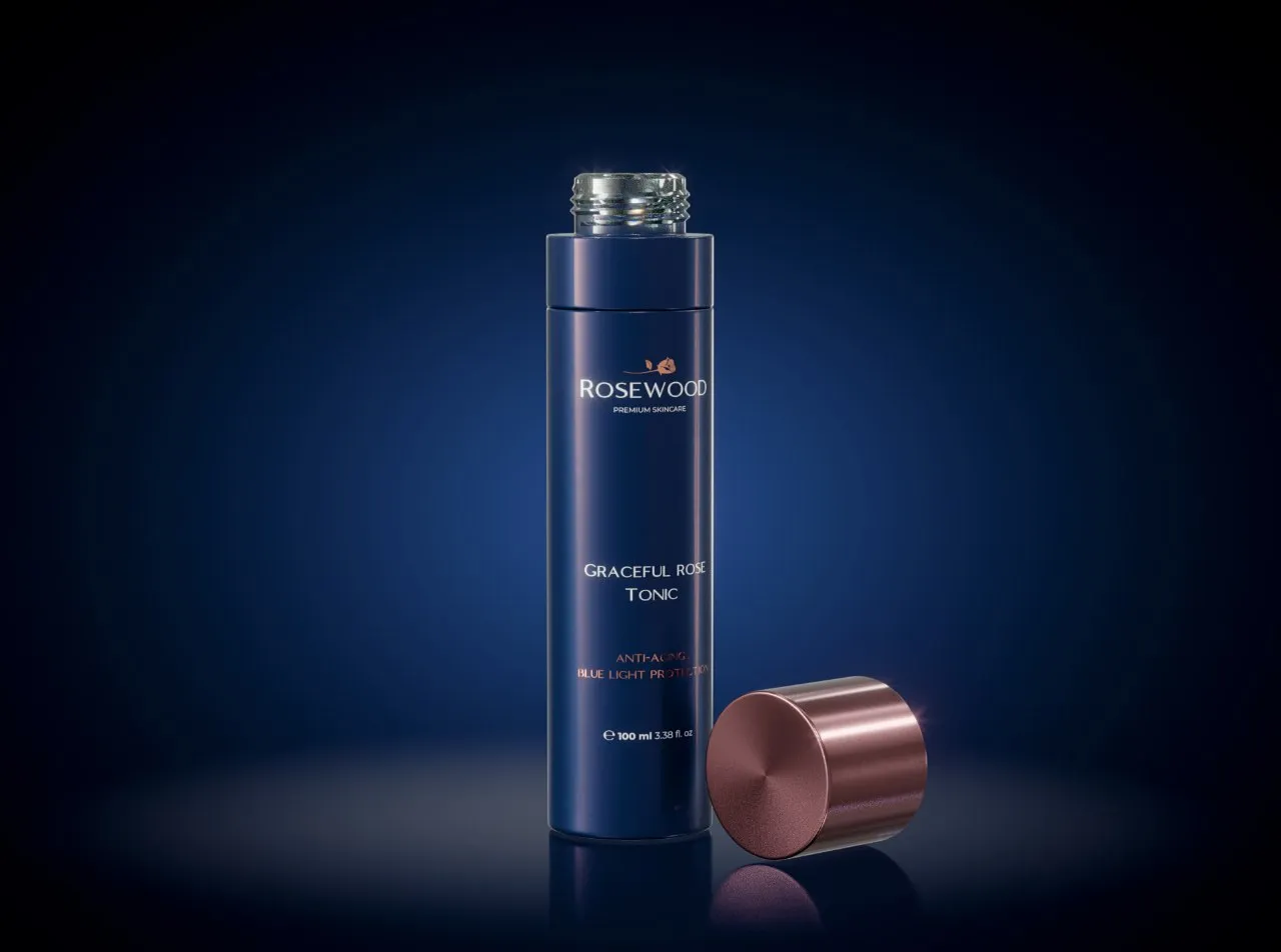 Uncapped navy Rosewood Graceful Rose Tonic bottle with its rose-gold cap resting alongside on a dark reflective surface
